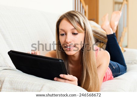 Barefoot girl laying on couch and reading something from tablet screen