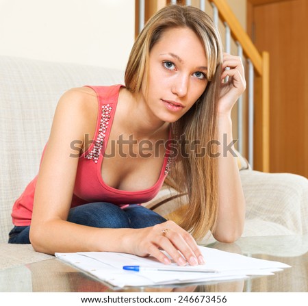 Thoughtful student girl sitting on the sofa with educational materials in the hands