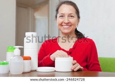 Happy mature woman doing cosmetic mask on her face at home interior
