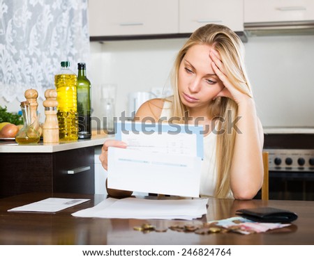 Sad blonde housewife filling in utility payments bills at home
