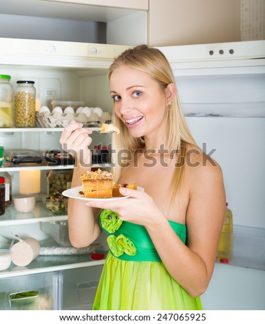 hungry woman near opening fridge eating cake in her home