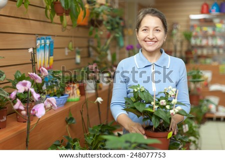 Happy mature woman looks Clerodendrum plant at flower store