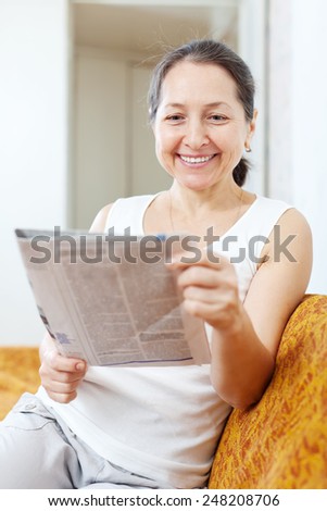 Smiling mature woman reads newspaper on sofa