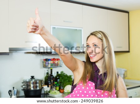 Smiling young female turned up the thumbs in kitchen