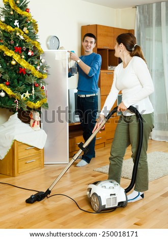 Happy man and woman cleaning with vacuum cleaner in Christmas time