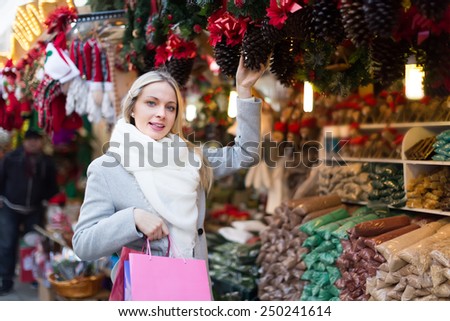 Happy smiling blonde young woman choosing Christmas decoration at market