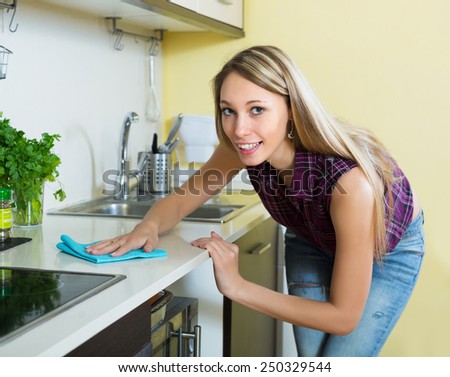 Smiling  young housewife cleaning furniture in kitchen