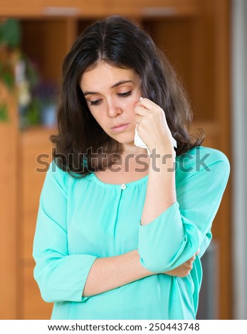 Young brunette woman crying at home wiping away tears with a handkerchief