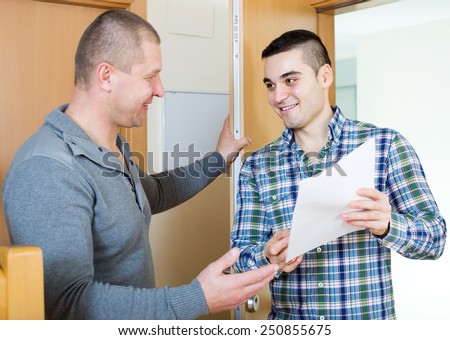 Young lodger talking neighbor with papers at doorway. Focus on the right man