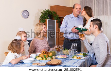 Smiling family member receiving present from relatives at table. Focus on mature woman
