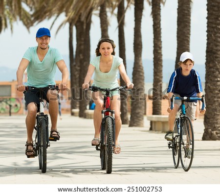 smiling family of three cycling over city in summer day