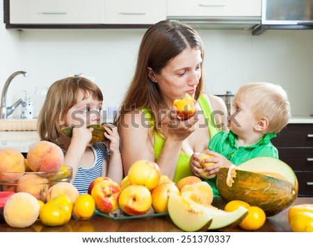 Happy woman with daughters together with melon and peaches over dining table at home interior
