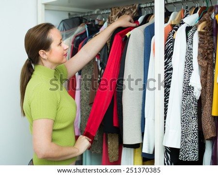 Middle-aged woman choosing apparel on shelves at store