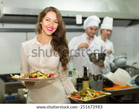 Beautiful smiling female waiter taking dish from kitchen in cafe Beautiful smiling female waiter taking dish from kitchen in cafe