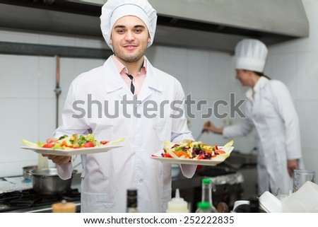 Two smiling cooks working together at restaurant kitchen. Focus on man