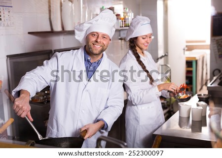 Two smiling cooks working together at kitchen in take-away restaurant
