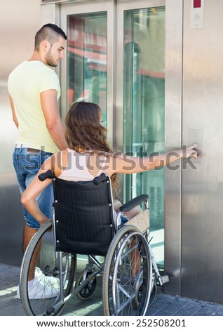Handsome european man helping handicapped girlfriend at outdoor elevator