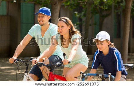 cheerful family of three cycling on city street in summer day