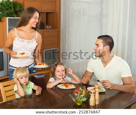 Happy parents and two children having lunch with spaghetti at home together. Focus on girl