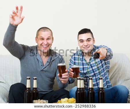 Two excited men drinking beer and watching football game indoor. Focus on one