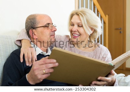Portrait of loving senior spouses smiling with picture album indoors