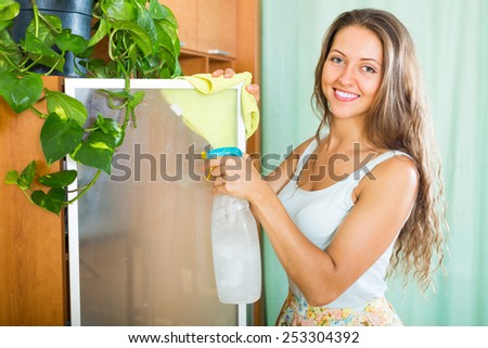 Smiling young brunette woman cleaning glass of furniture at home