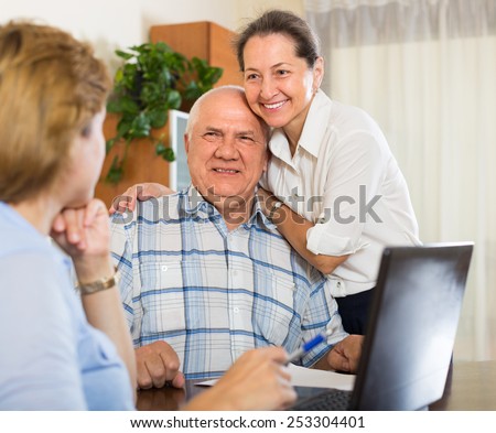 Smiling senior couple answer questions of social worker at home. Focus on man
