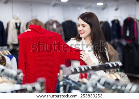 Happy female buyer choosing sweater at clothing store