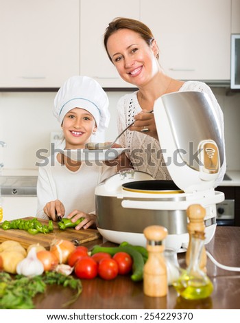 Portrait of smiling little girl and her mom with rice cooker. Focus on girl
