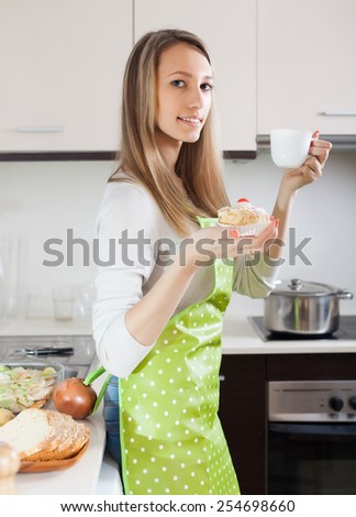 Woman in apron eating  cakes with tea in home kitchen