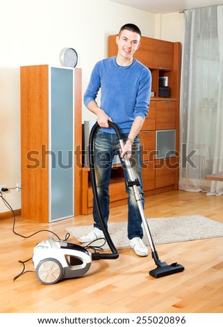 Ordinary guy  vacuuming with vacuum cleaner on parquet floor in home