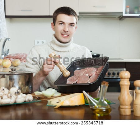 Handsome man cooking  meat . Adding raw meat in roasting pan
