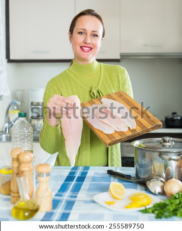 Happy woman cooking soup with filleted fish at kitchen
