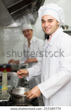 Two smiling professional cooks working at restaurant kitchen. Focus on man