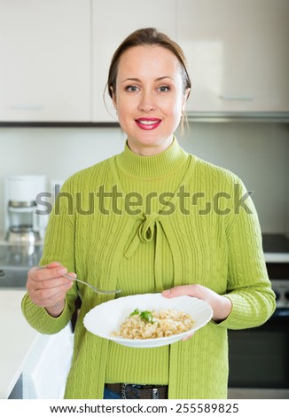 Smiling russian woman in green eats rice at kitchen