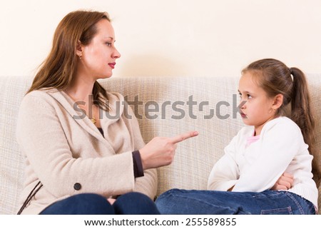 Angry mother showing finger to schoolgirl daughter indoor