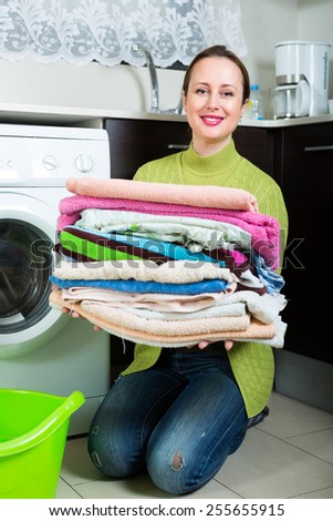 Home laundry. Smiling woman in green loading clothes into washing machine in home