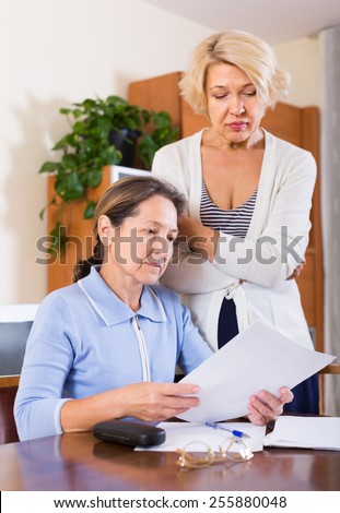 Upset female pensioners reading documents with sad faces. Focus on brunette