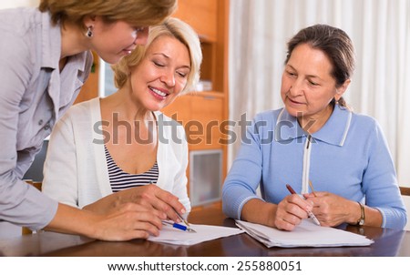 Two smiling positive female pensioners signing documents with public notary