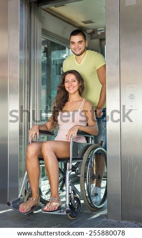Handsome man 20-25 years old helping handicapped girlfriend at outdoor elevator