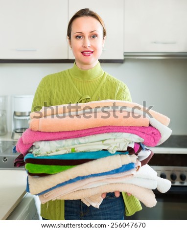 Woman doing laundry indoors. She is standing near washing machine and holding a heap of clean towels in her hands
