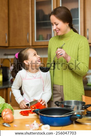 Happy mother and preschooler daughter preparing soup together at home kitchen and smiling. Focus on girl