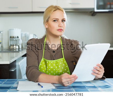 Serious blonde girl reading document at kitchen