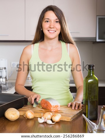 Happy smiling girl cooking salmon fish in frying pan at kitchen