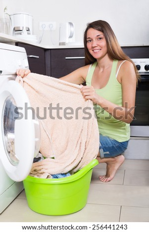 Home laundry. Happy young  smiling  woman loading clothes into washing machine  in home