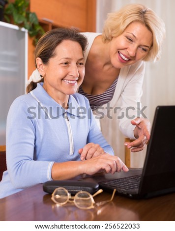 Smiling senior ladies with laptop buying something online. Focus on brunette