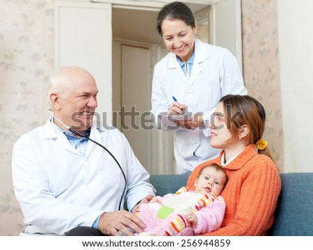 Doctor examining newborn baby on mother\'s arms in house. Mature nurse writes symptoms