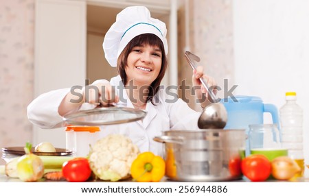 Happy  woman in toque cooks from vegetables with ladle