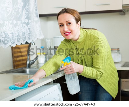 Smiling brunette woman cleaning furniture at home  kitchen