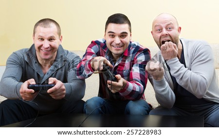 Three shouting european friends playing video games at house party